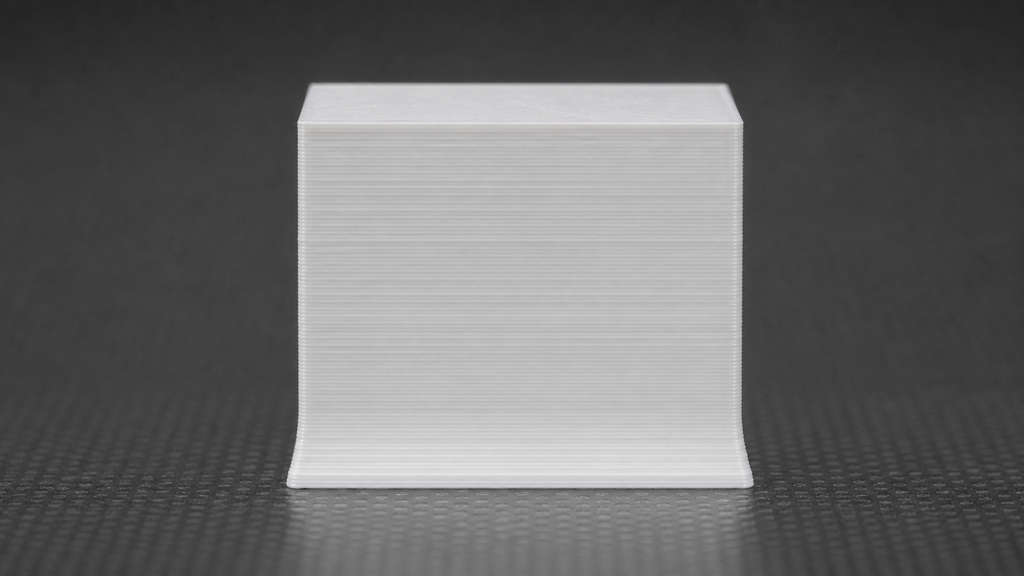 Close-up of a white calibration block whose first few layers flare beyond the straight walls above.