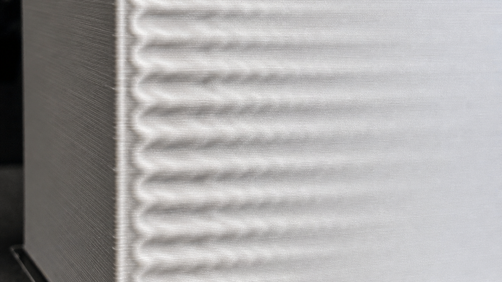 Close-up of a white wall with repeated ripples trailing a sharp printed feature.