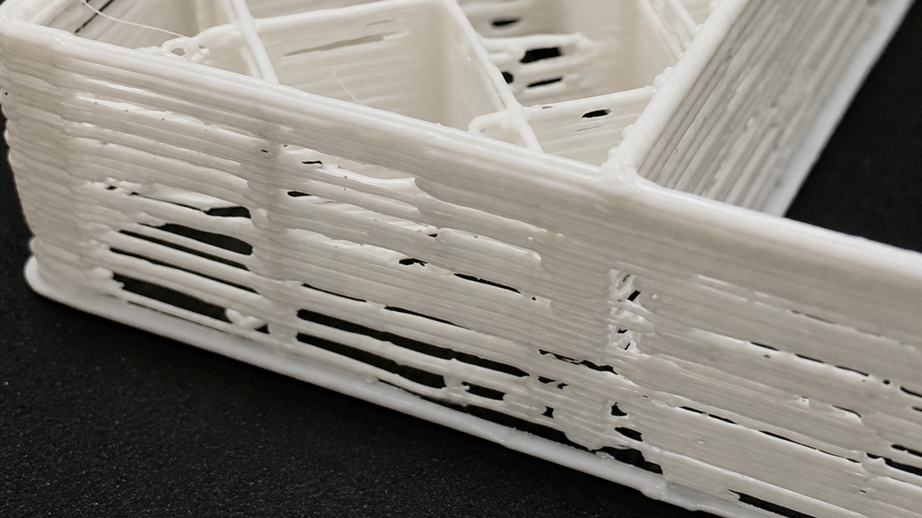 Close-up of a white printed part with gaps and separated extrusion lines in its walls.